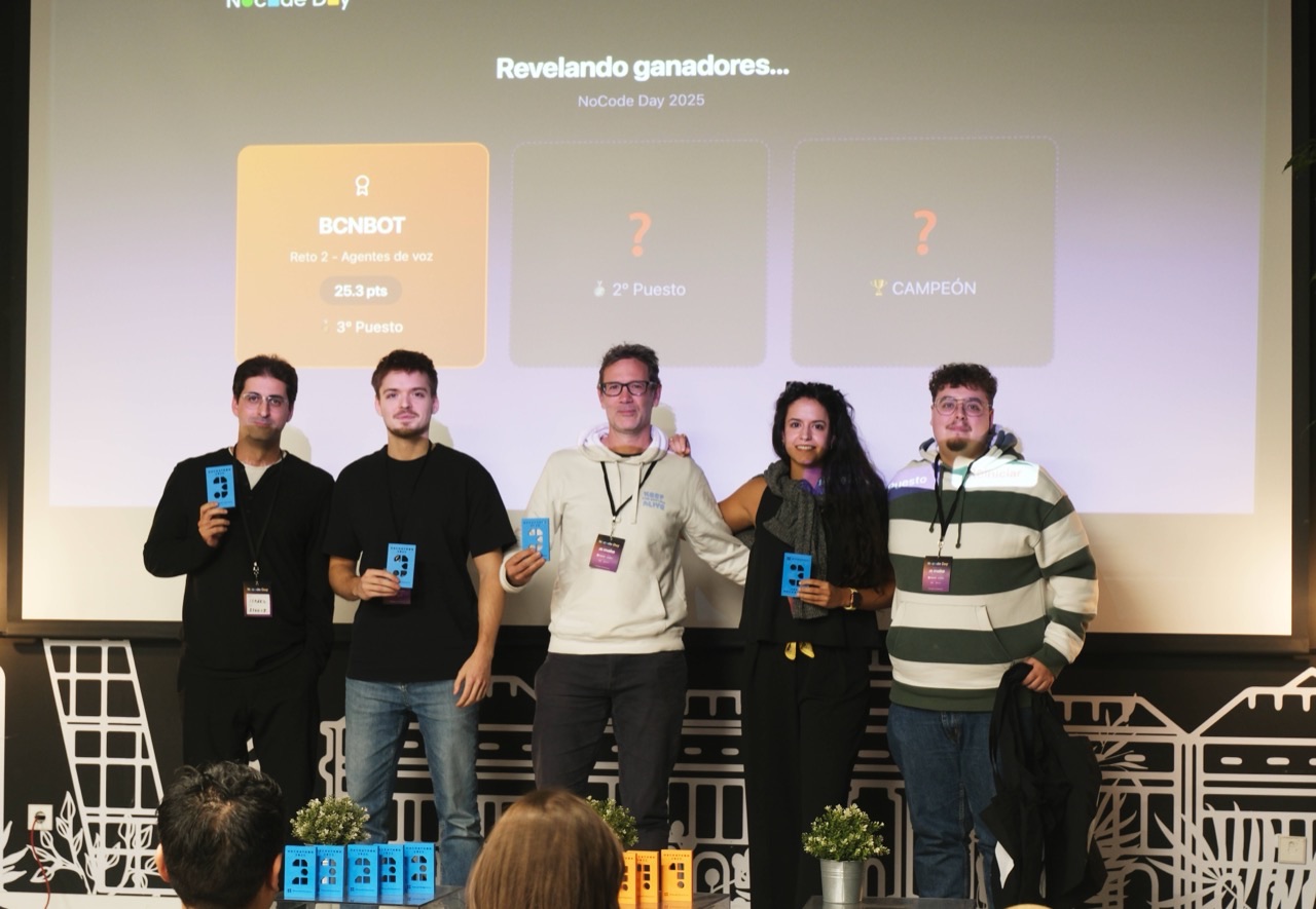 Cinco participantes posan con sus acreditaciones delante de la pantalla «Revelando ganadores… NoCode Day 2025», que muestra al equipo BCNBOT en tercer puesto.